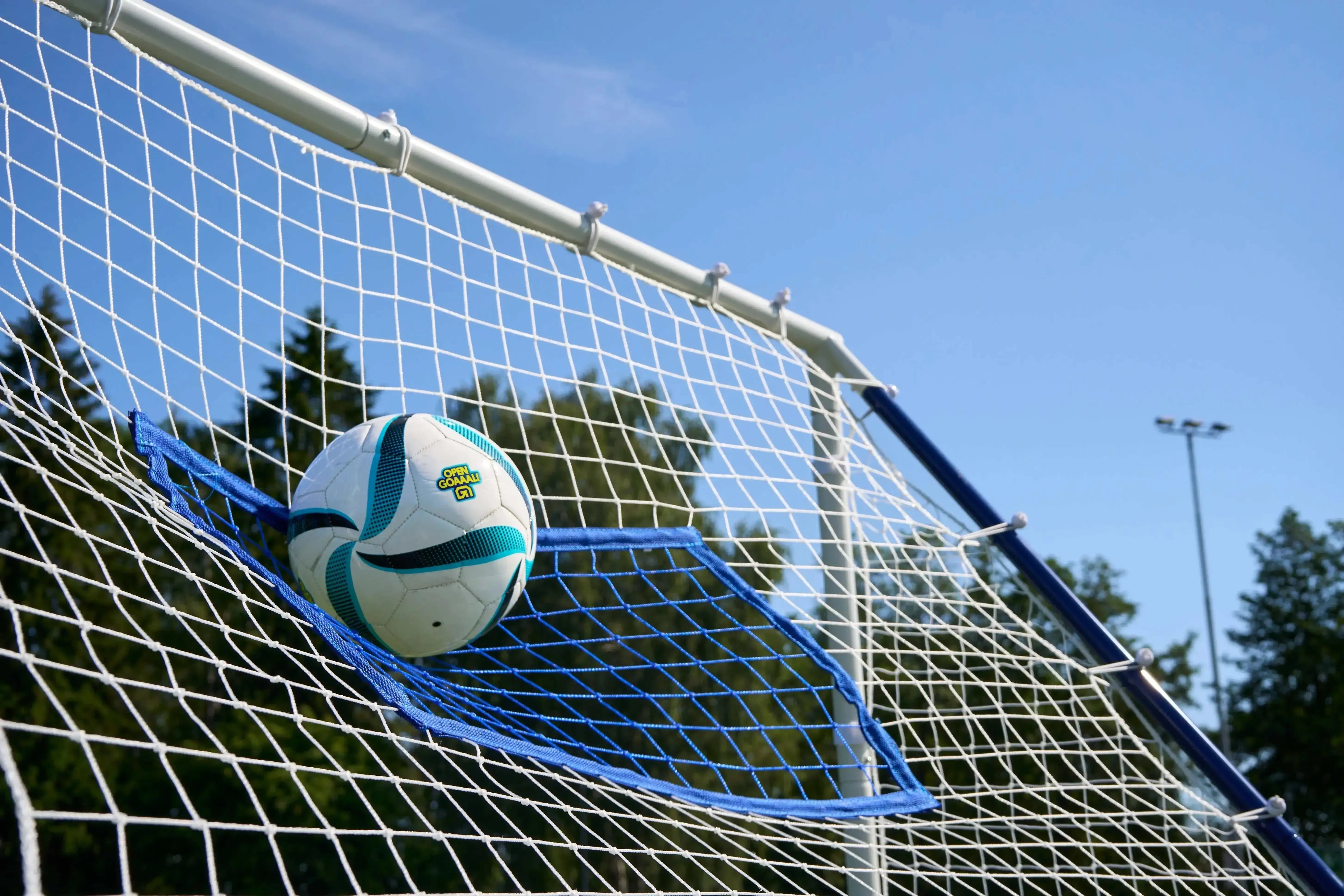 Football in a goal net under a blue sky, showcasing the excitement of soccer training and gameplay.